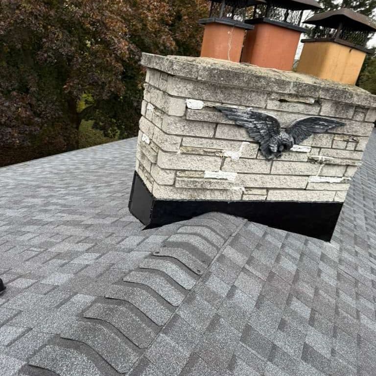 Stone chimney with new black flashing and a cast eagle, finished in gray shingles