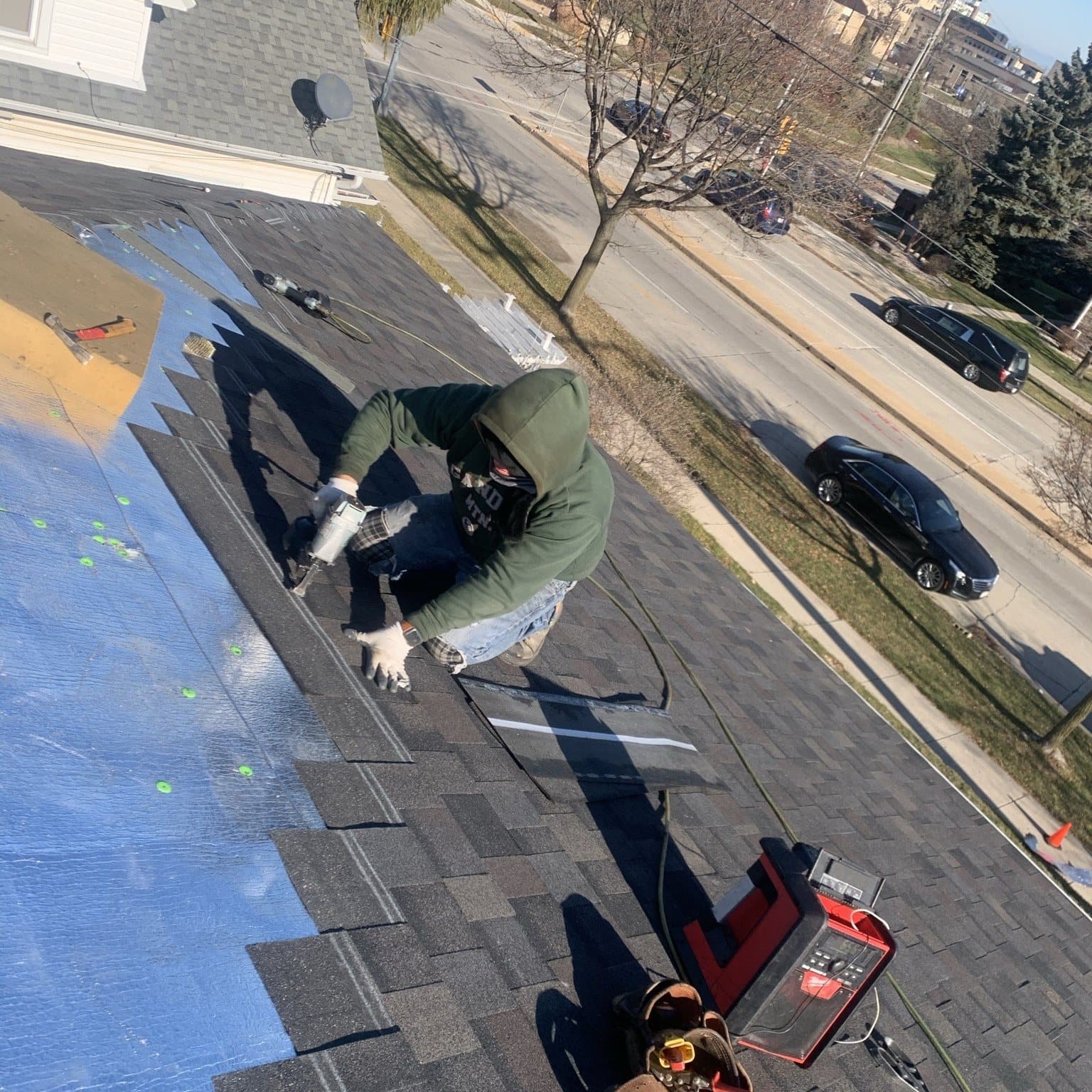 Roofer installing shingles with a nail gun over synthetic underlayment